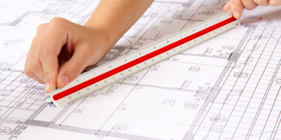 Two hands using a scale ruler on a set of blueprints